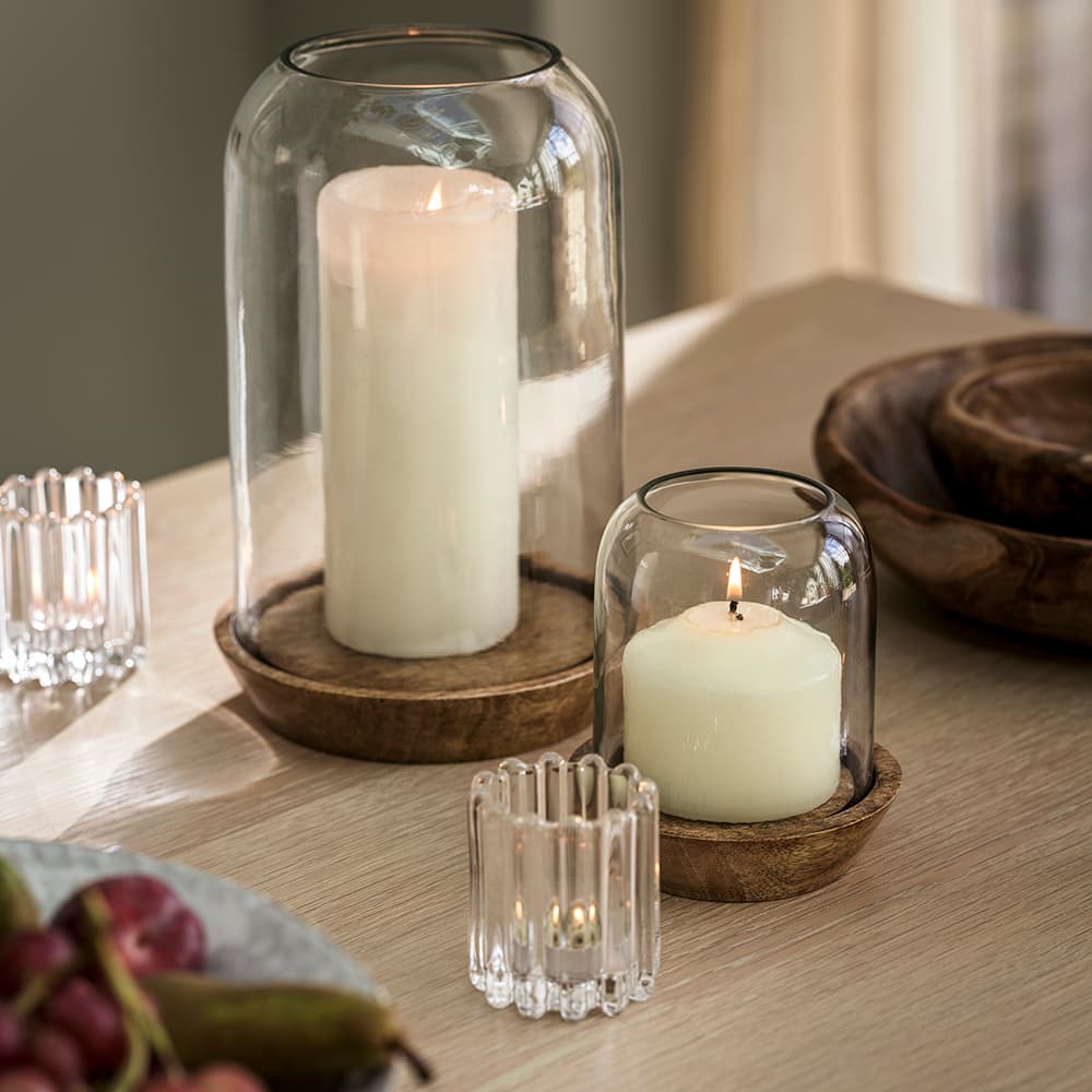 Two candles in glass holders on a wooden table, surrounded by small glass votives.
