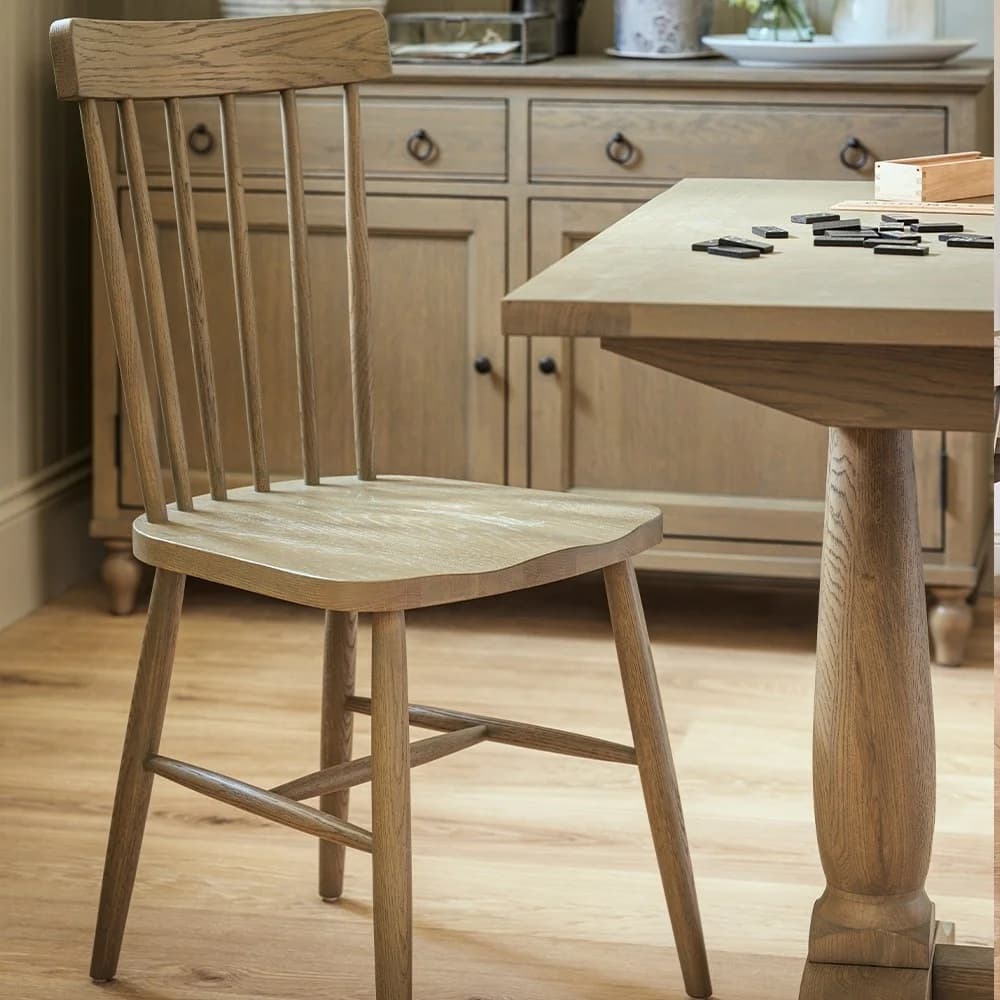 Wooden chair beside a table with scattered dominoes, set in a rustic kitchen with wooden flooring and cabinets.