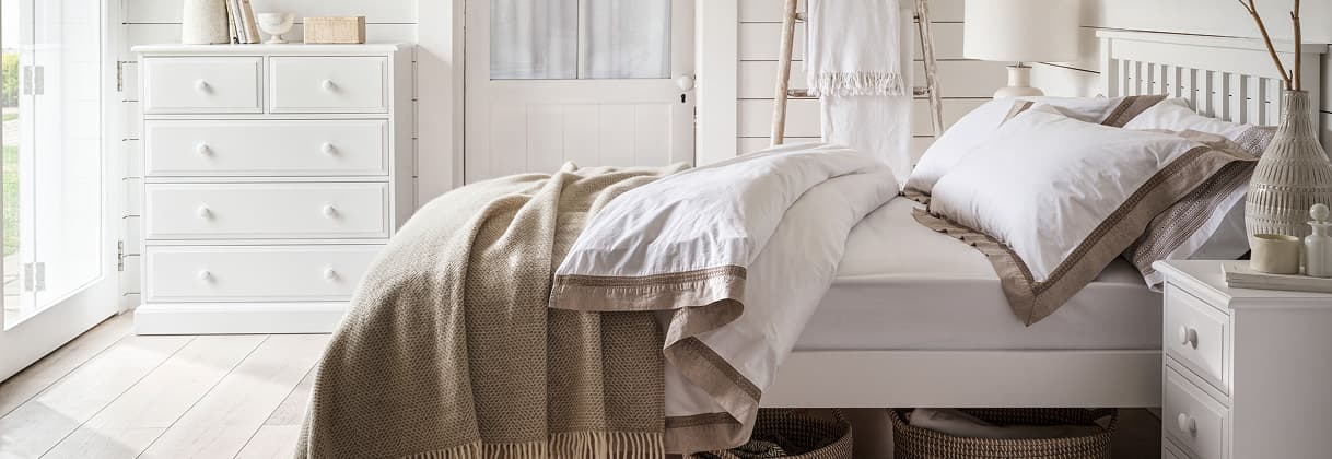 Cozy bedroom with a white wooden bed, beige and white bedding, a dresser, and baskets underneath.