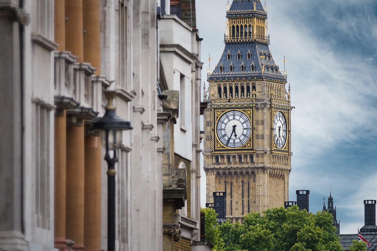 View of Big Ben with its clock face, surrounded by historic buildings and greenery against a partly cloudy sky.