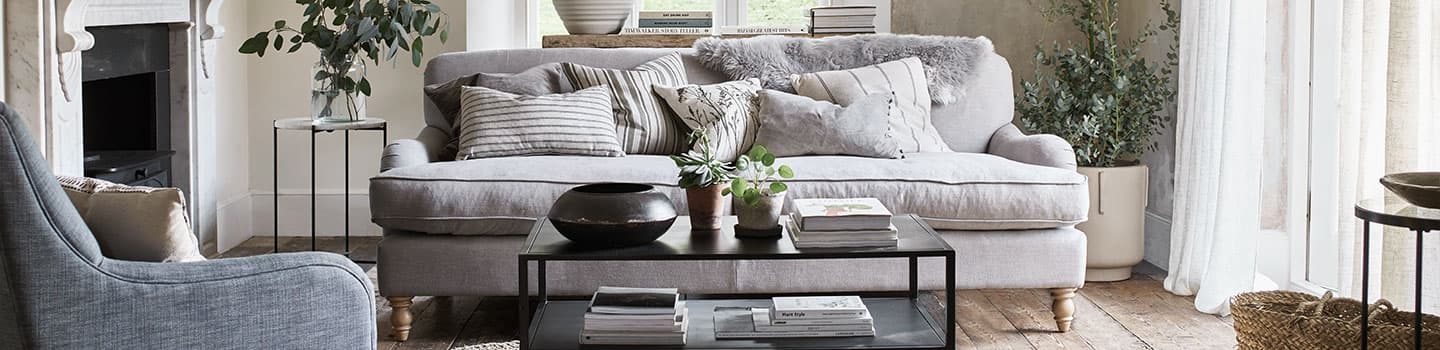 Cozy living room with a gray sofa, assorted pillows, a black coffee table, plants, and a soft armchair, all in neutral tones.