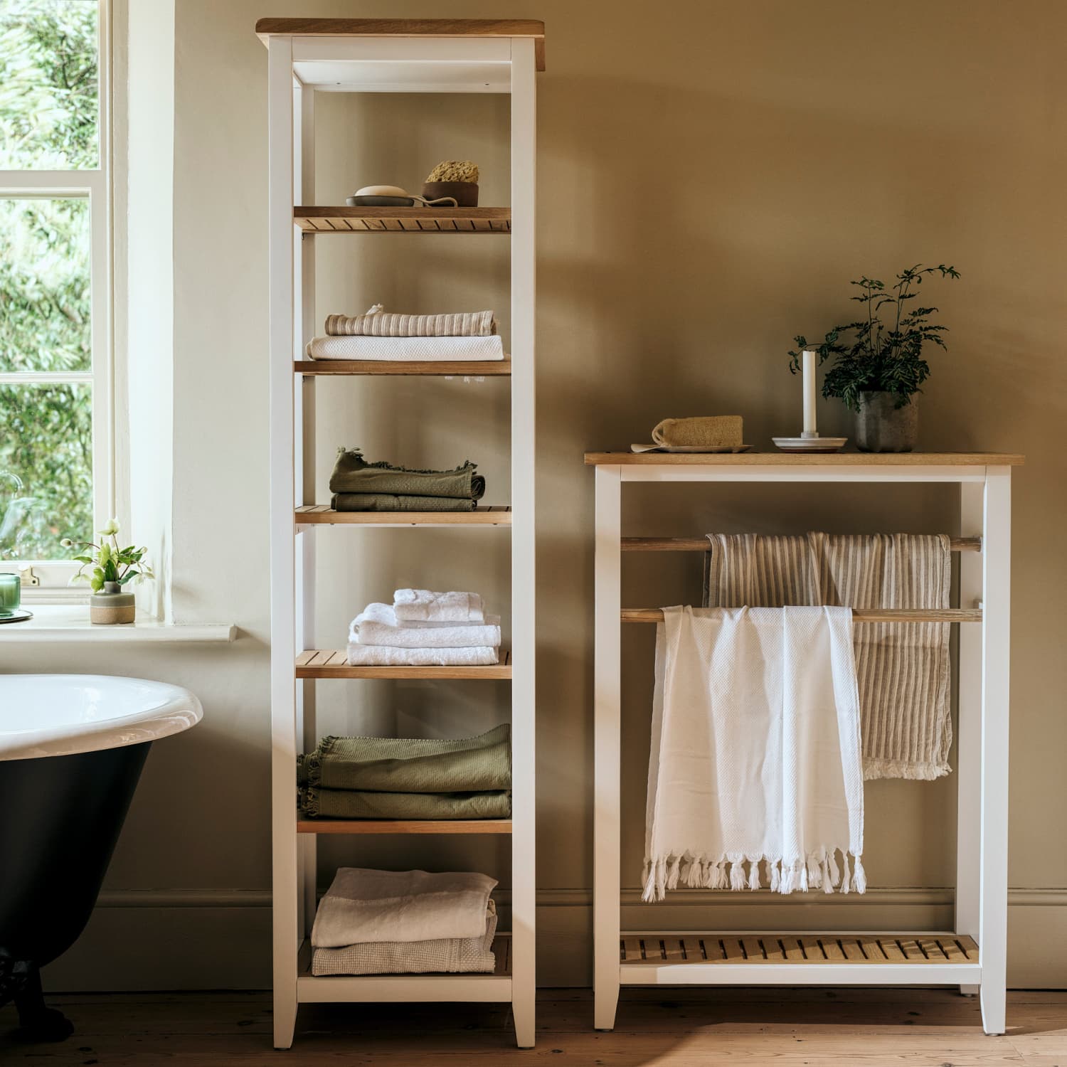 Wooden bathroom shelves filled with neatly folded towels, a plant, and a candle beside a window with natural light.
