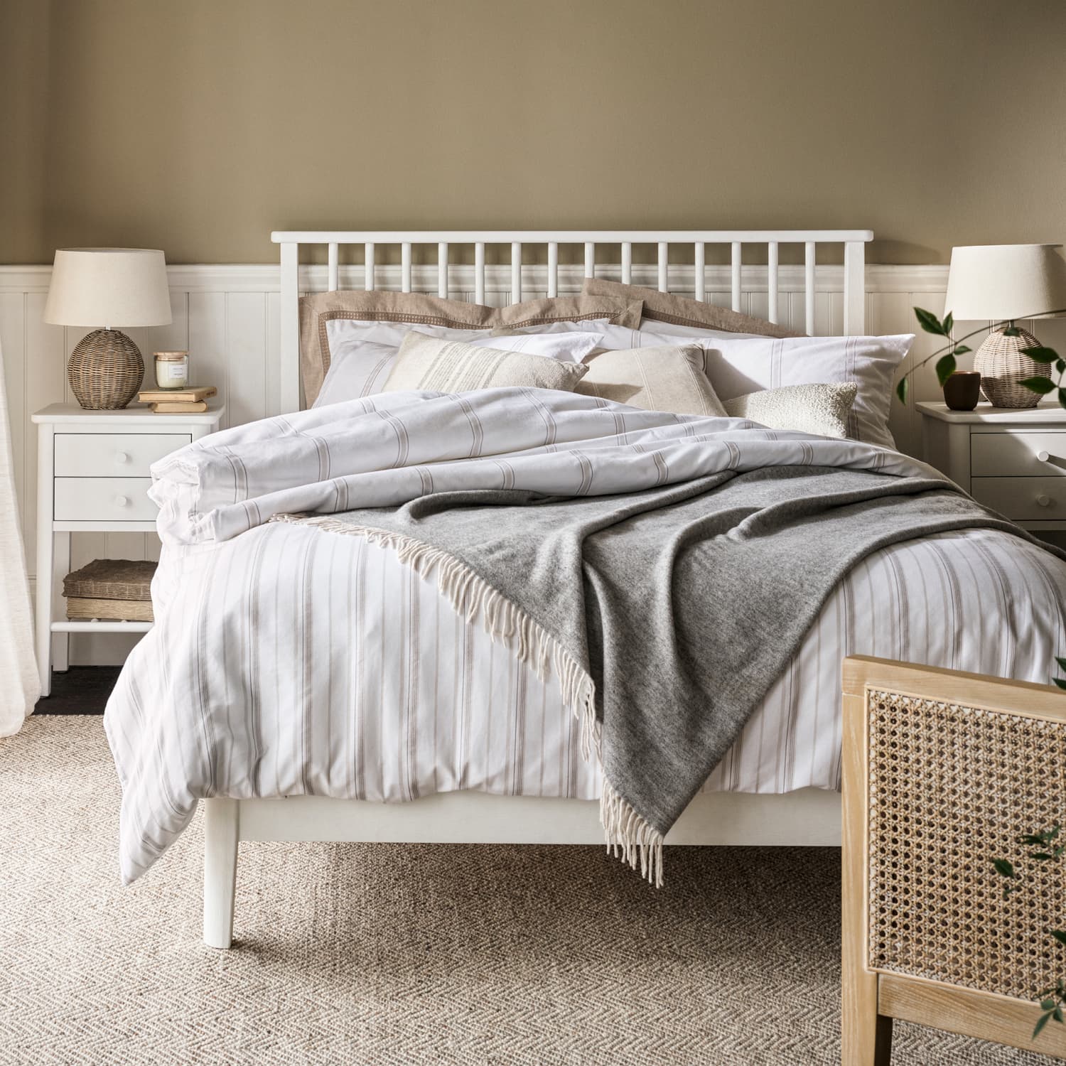 Bedroom with a white bed, striped bedding, grey throw blanket, and neutral-toned pillows, flanked by white nightstands and lamps.