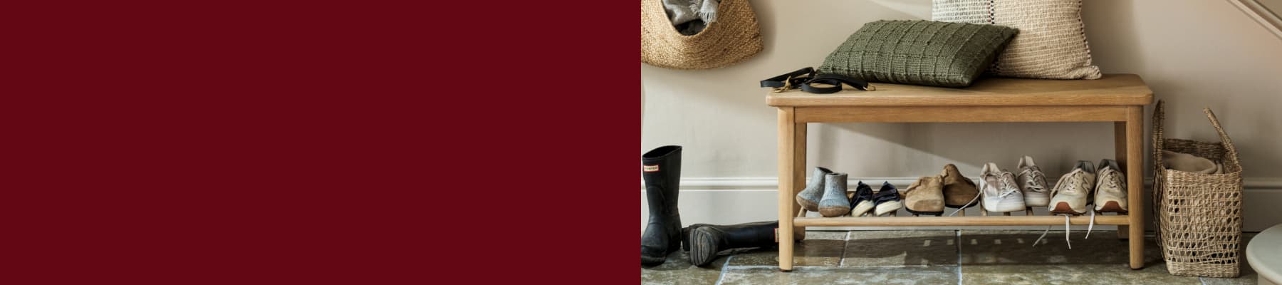 Wooden bench with pillows on top and various shoes underneath. A basket hangs on the wall, with boots and a wicker basket nearby.
