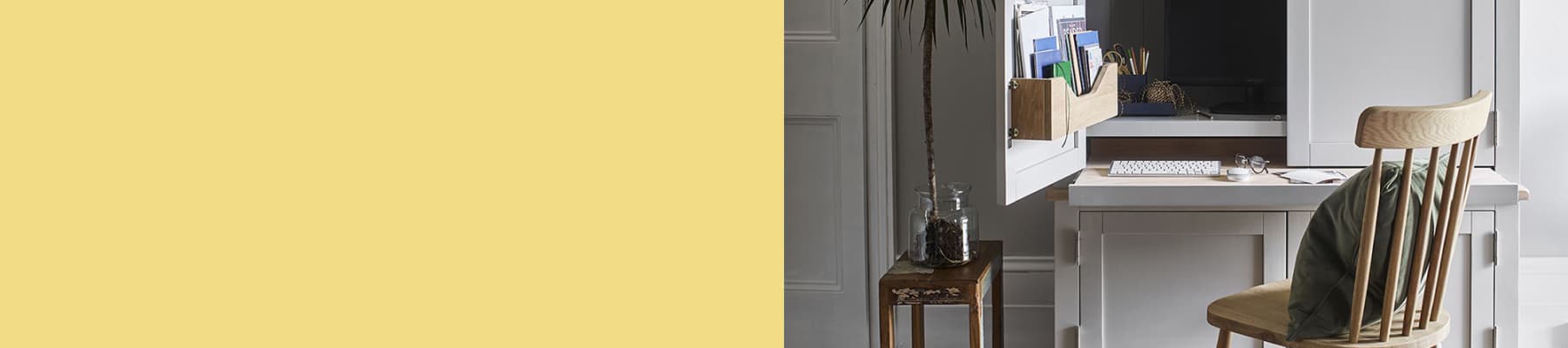 A home office setup with a wooden chair, desk, laptop, potted plant, and a glass jar on a small table.
