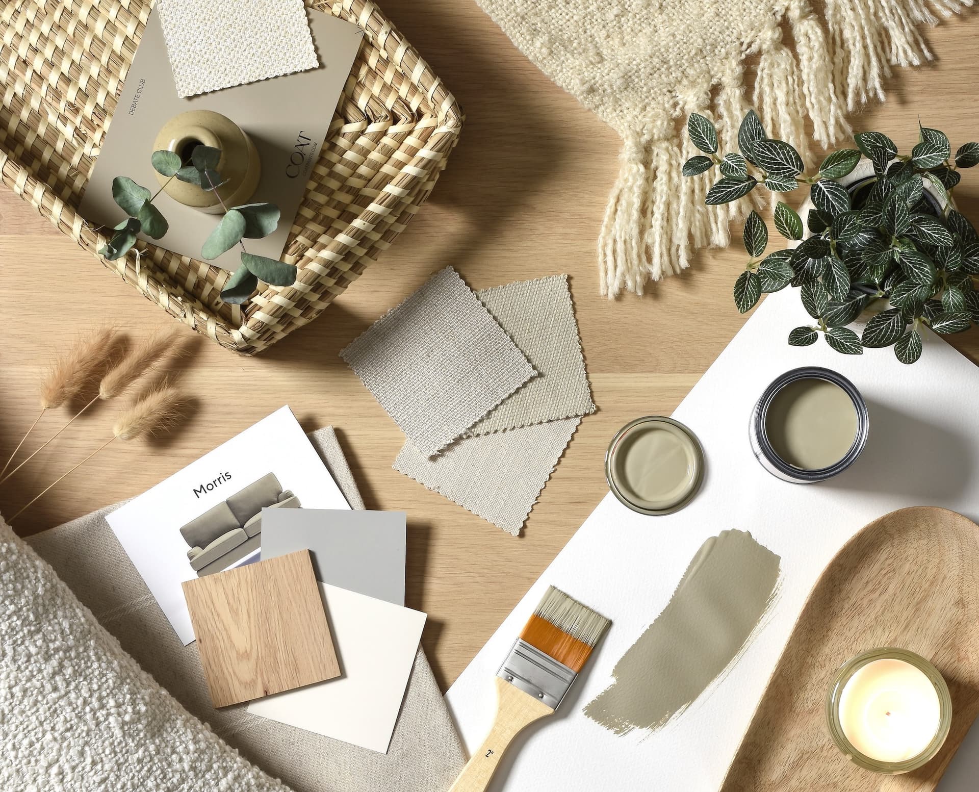 Home decor flat lay with fabric swatches, paint samples, a brush, wooden tray, small potted plant, candle, and a woven basket.
