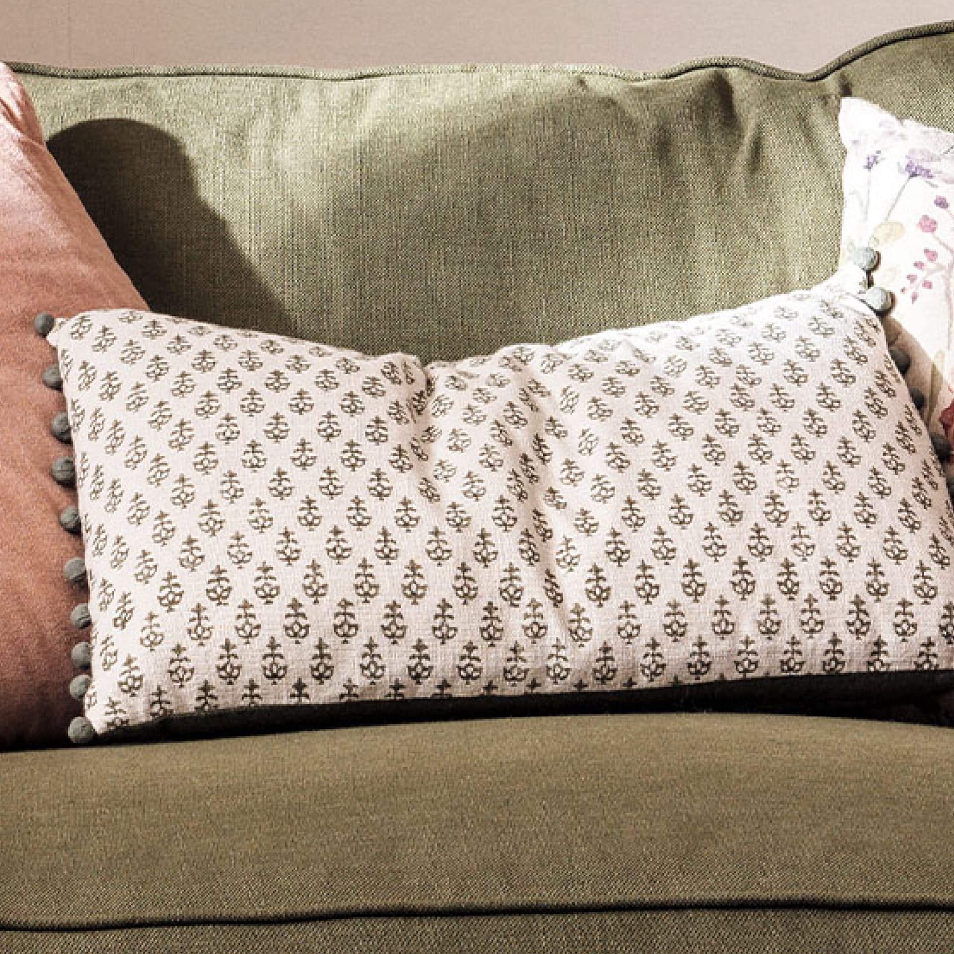 A green couch with a patterned white cushion and a pink pillow on the side.