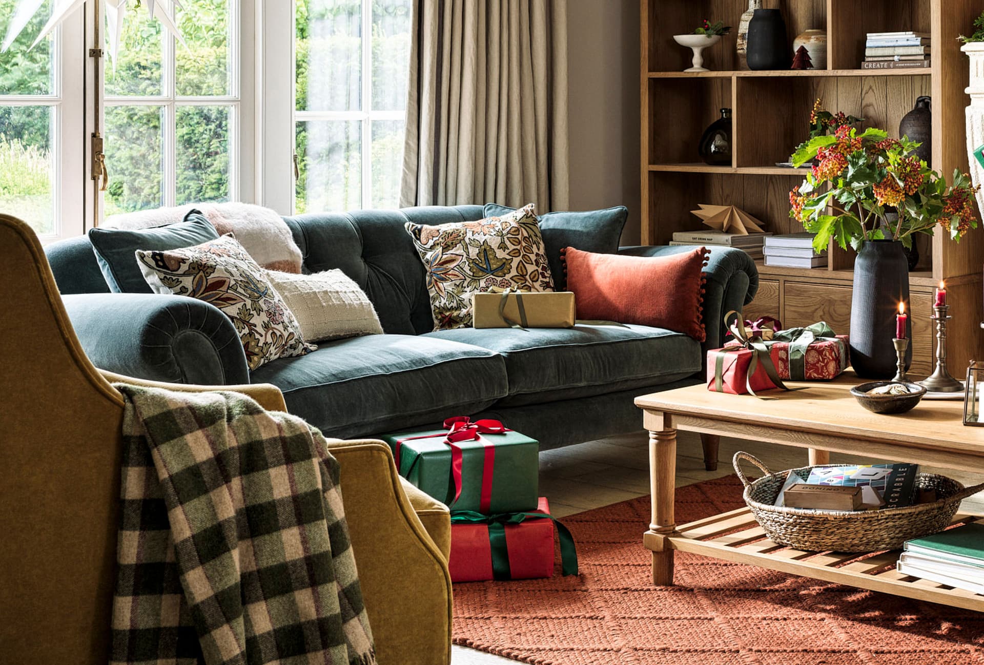 Cosy living room with a teal sofa adorned with patterned cushions, a coffee table with wrapped gifts, and a vibrant floral arrangement.