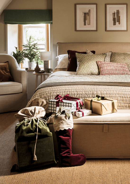 Cosy bedroom decorated with Christmas gifts and stockings at the foot of the bed. Soft lighting and neutral tones create a warm, festive atmosphere.