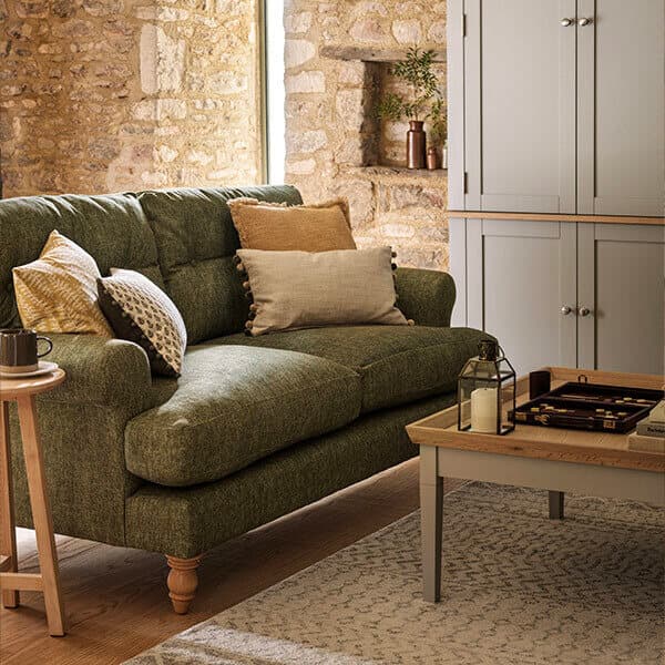 Cozy living room with a green sofa, assorted pillows, wooden coffee table, stone wall, and a cabinet. Warm, inviting atmosphere.