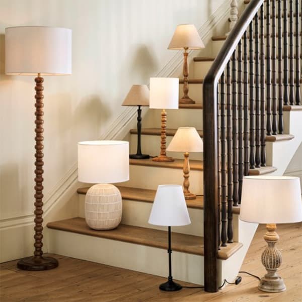 A variety of table and floor lamps with different designs are displayed on wooden stairs and floor, against a neutral-colored wall.