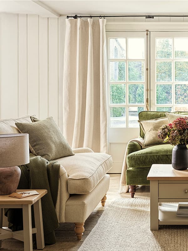 Living room with neutral armchair, green sofa, floral arrangement on coffee table, and French doors letting in natural light.