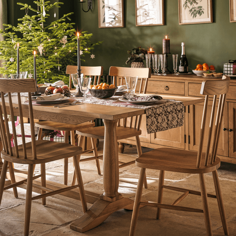 Dining room with a wooden table set for a meal, surrounded by chairs, a decorated Christmas tree, and candlelit ambiance.