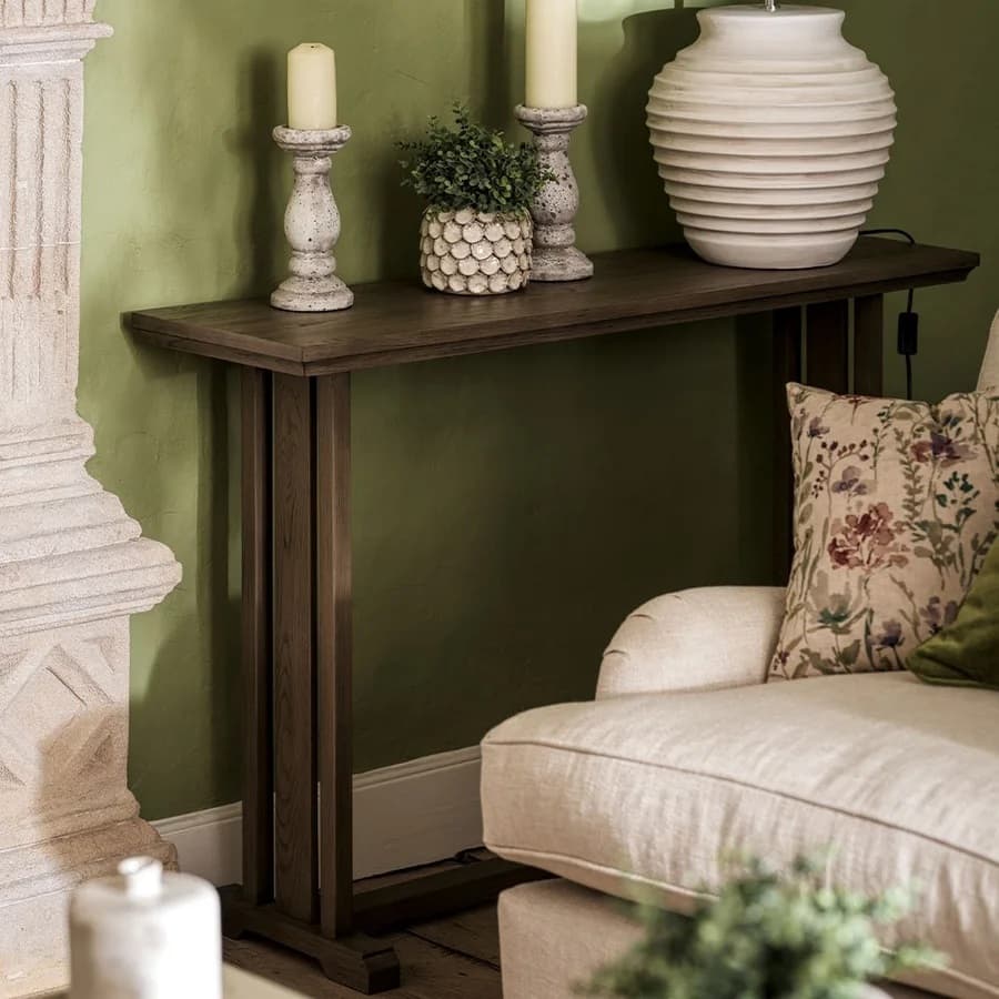 A living room corner with a wooden console table, candles, a vase, and a decorative pot. A stone fireplace and floral pillow on a beige sofa are visible.