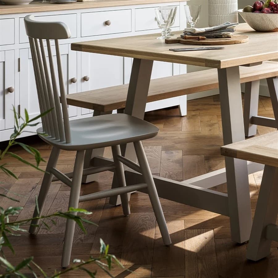 A wooden dining table with a gray chair and bench on a herringbone wood floor. White cabinets and a countertop with tableware are visible.