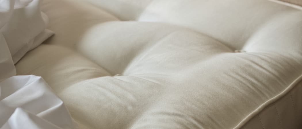 Close-up of a beige tufted mattress with a soft, smooth surface, partially covered by white sheets.