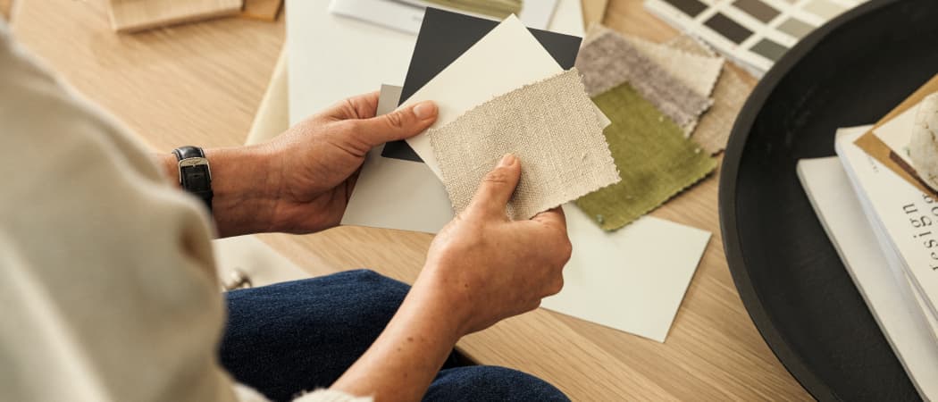 Person holding fabric and color swatches over a wooden table, surrounded by design samples and books.