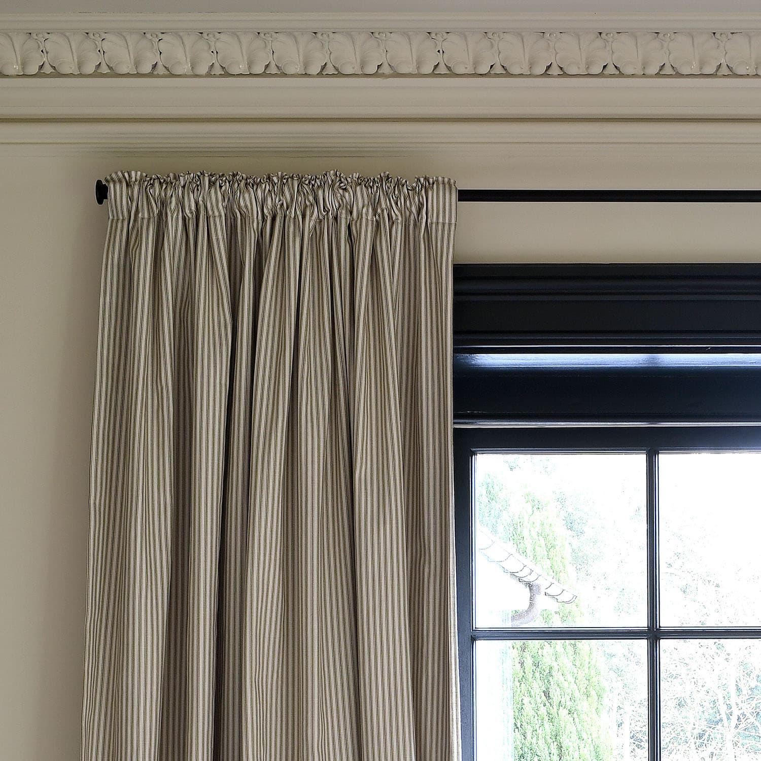 Striped curtains hang near a tall window with a black frame, under an ornate, decorative white ceiling molding.