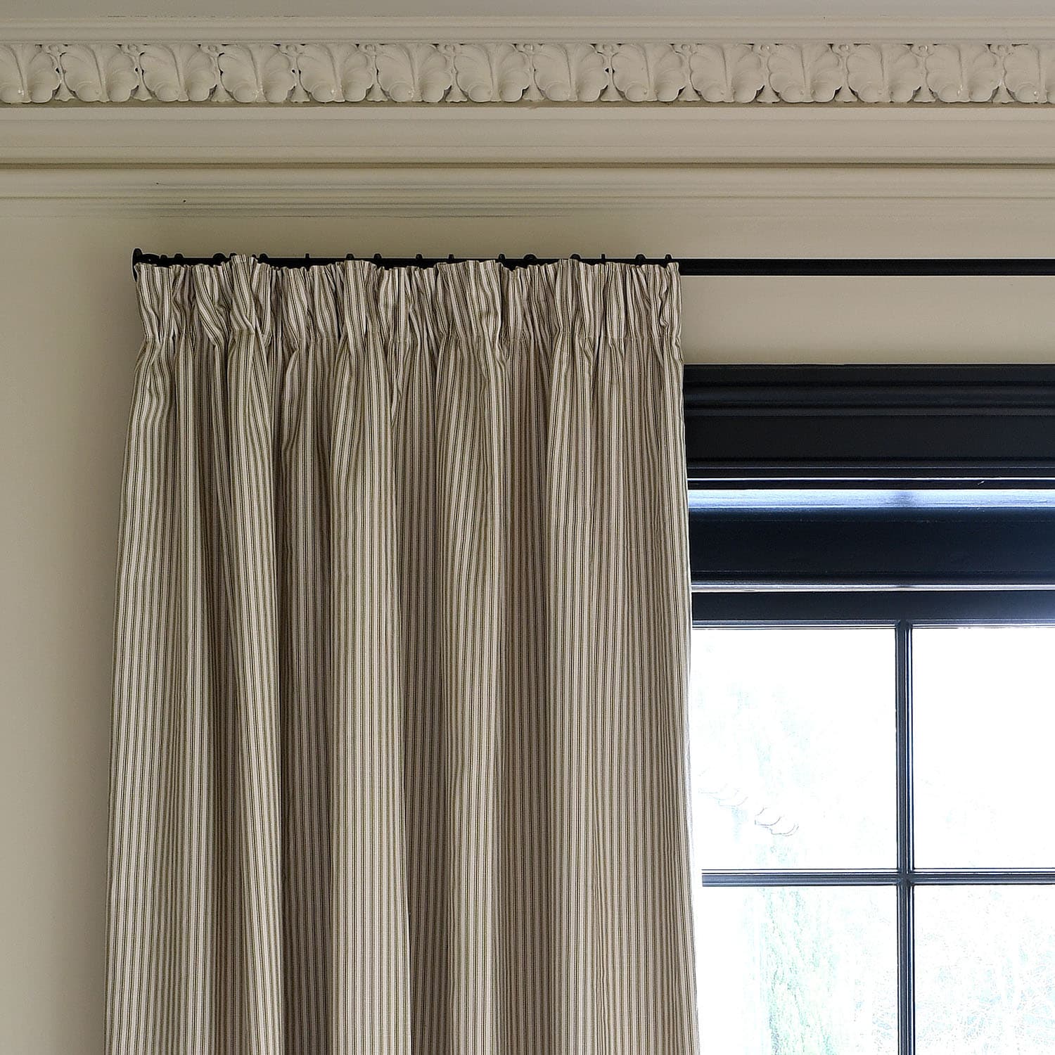 Striped curtains hanging next to a black window frame in a room with decorative molding.