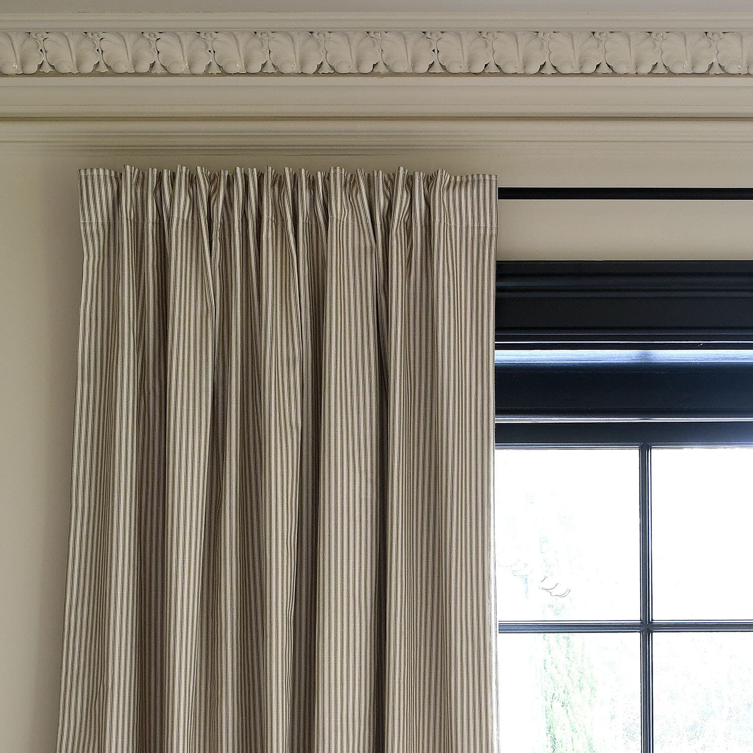 Striped curtains hanging next to a window, with an ornate molding detail above.