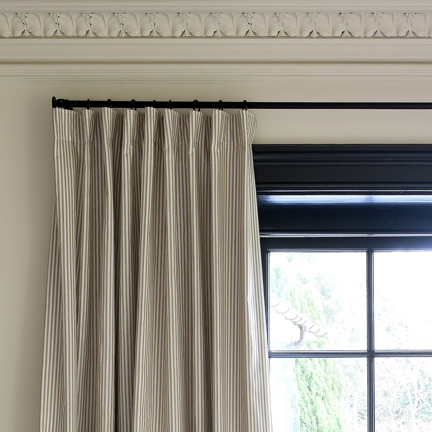 Elegant striped curtains hang from a black rod next to a large window, framed by ornate crown molding.