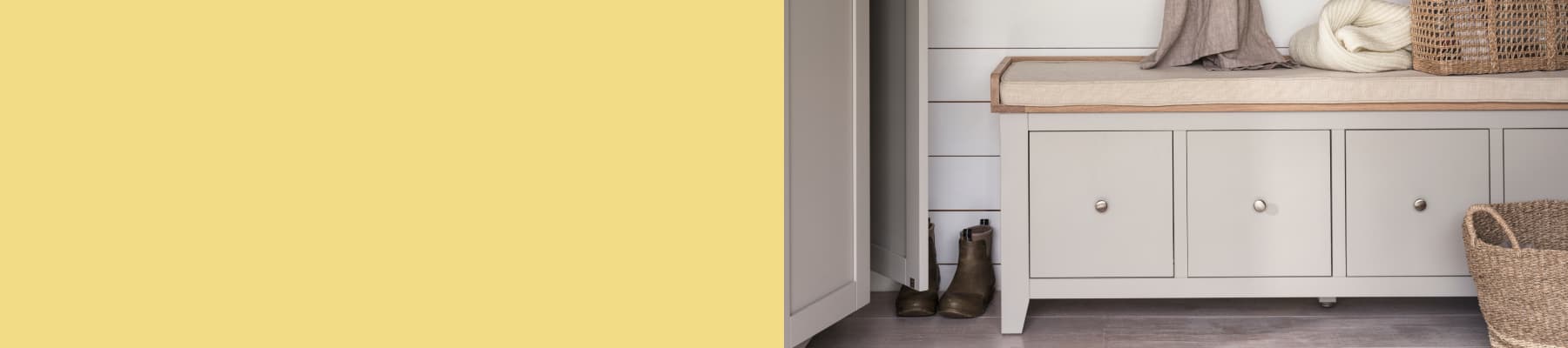 An entryway with a cushioned bench, wicker basket, folded blankets and a pair of boots.