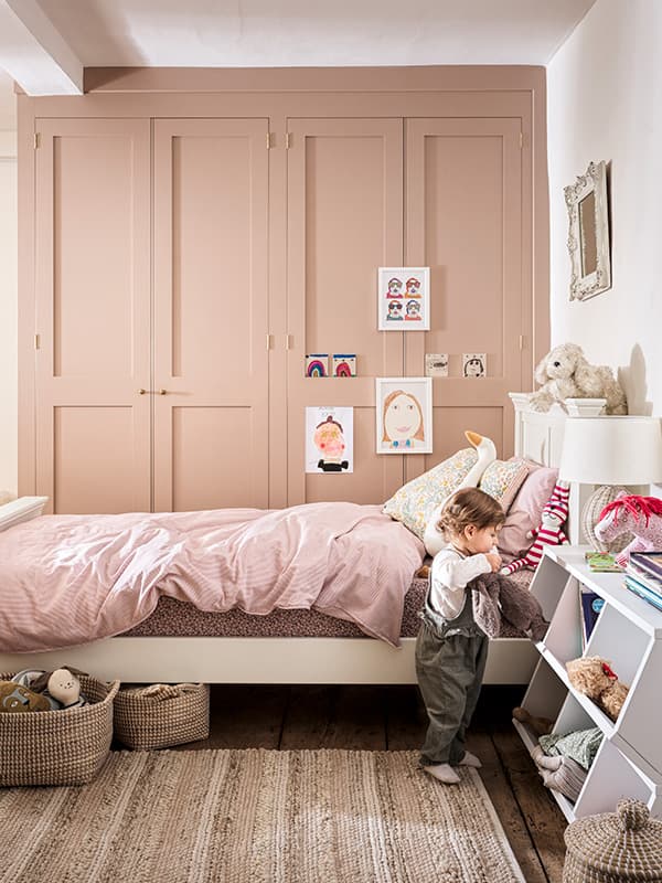 Children's bedroom with soft pink decor and toddler going through toys