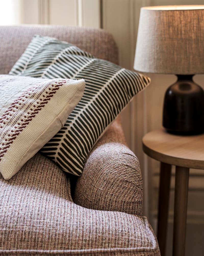 A sofa with textured cushions, striped and patterned, next to a wooden side table with a table lamp.