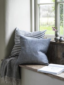 Window seat with blue cushions, throws and a book for a cosy corner.